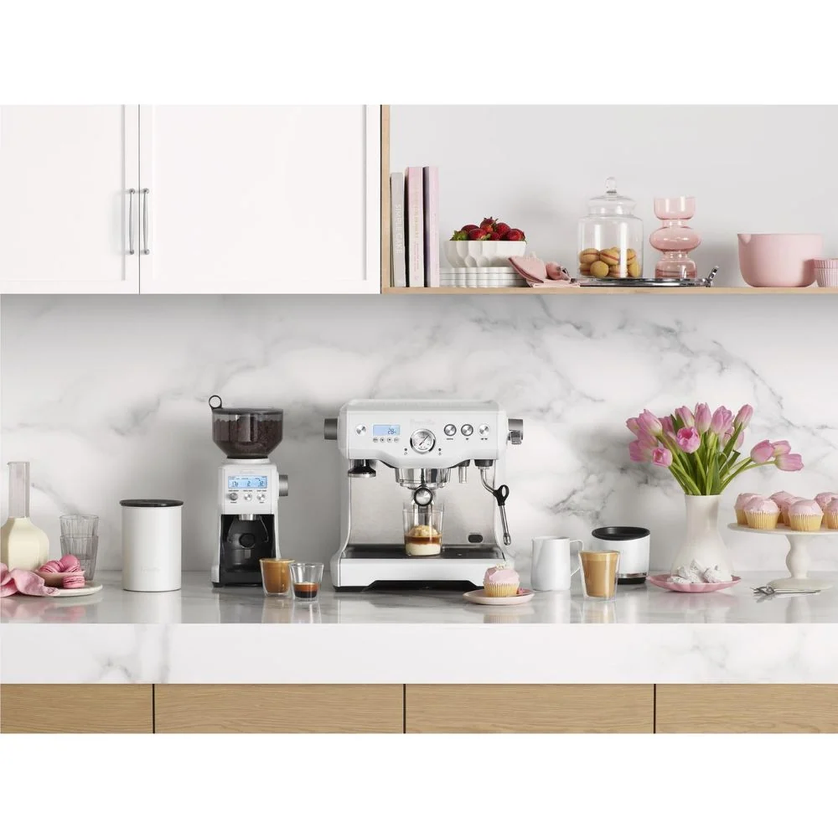White espresso machine with a pressure gauge and matching coffee grinder on a marble kitchen benchtop.