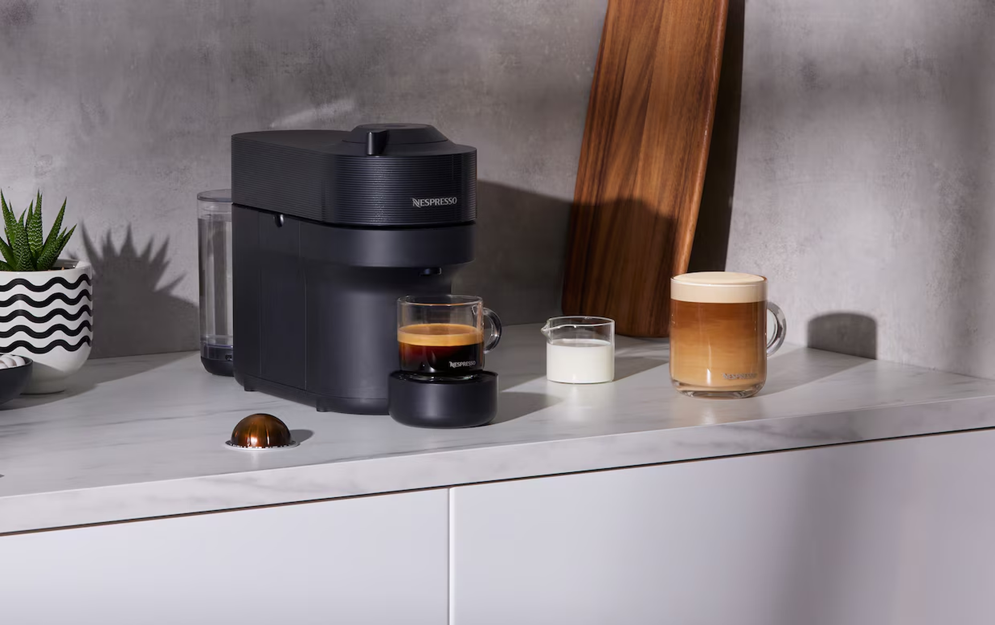 Black Nespresso coffee machine with espresso, milk and latte on a modern kitchen bench in New Zealand.
