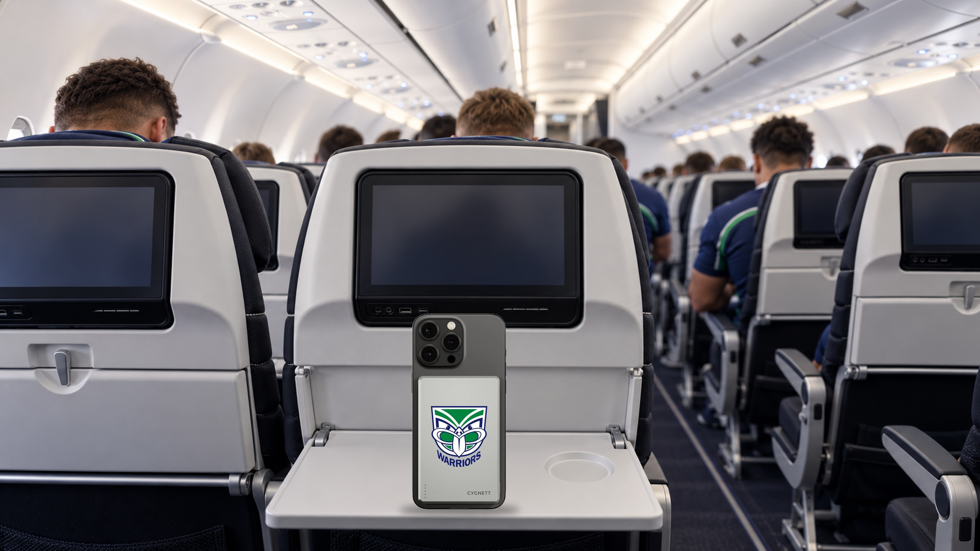 Cygnett Warriors power bank attached to a smartphone on an aircraft tray table, with an illustrated Warriors rugby league team seated ahead and viewed from behind - Power Banks at Tech Supply Shed NZ