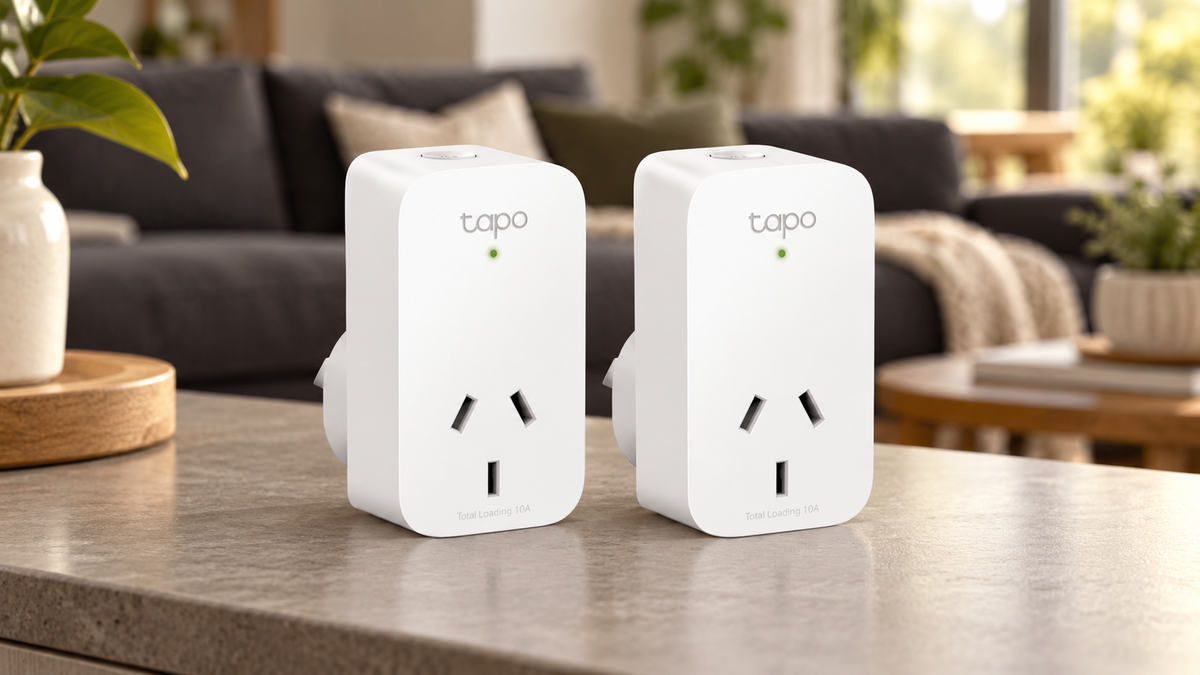 Two white Tapo smart plugs on a tabletop in front of a softly blurred modern lounge.