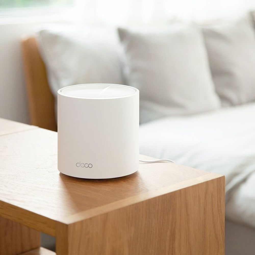 White Deco mesh WiFi node on a wooden table beside a couch