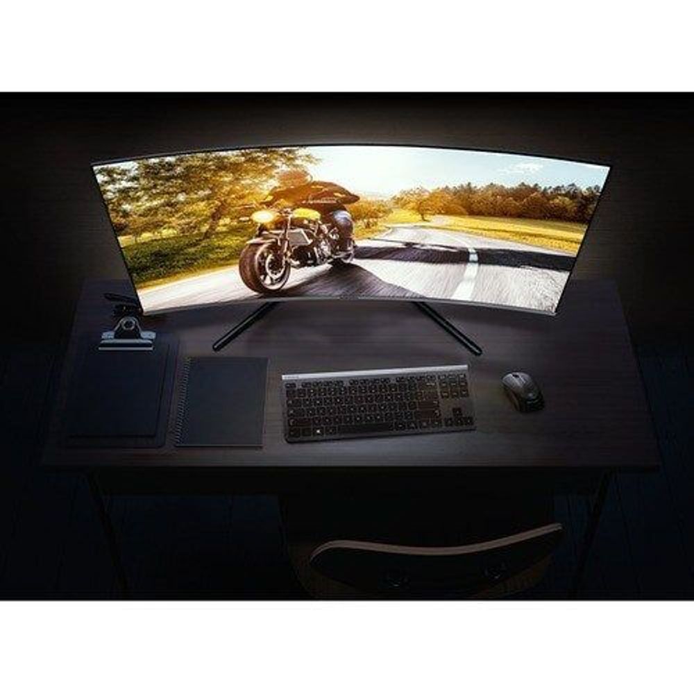 Samsung curved UHD LED monitor displaying motorcycle image with keyboard on desk