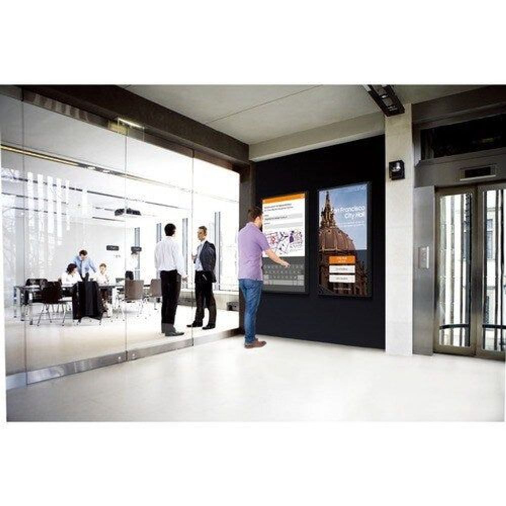 Touchscreen digital signage display mounted in office corridor, showing presentation slide