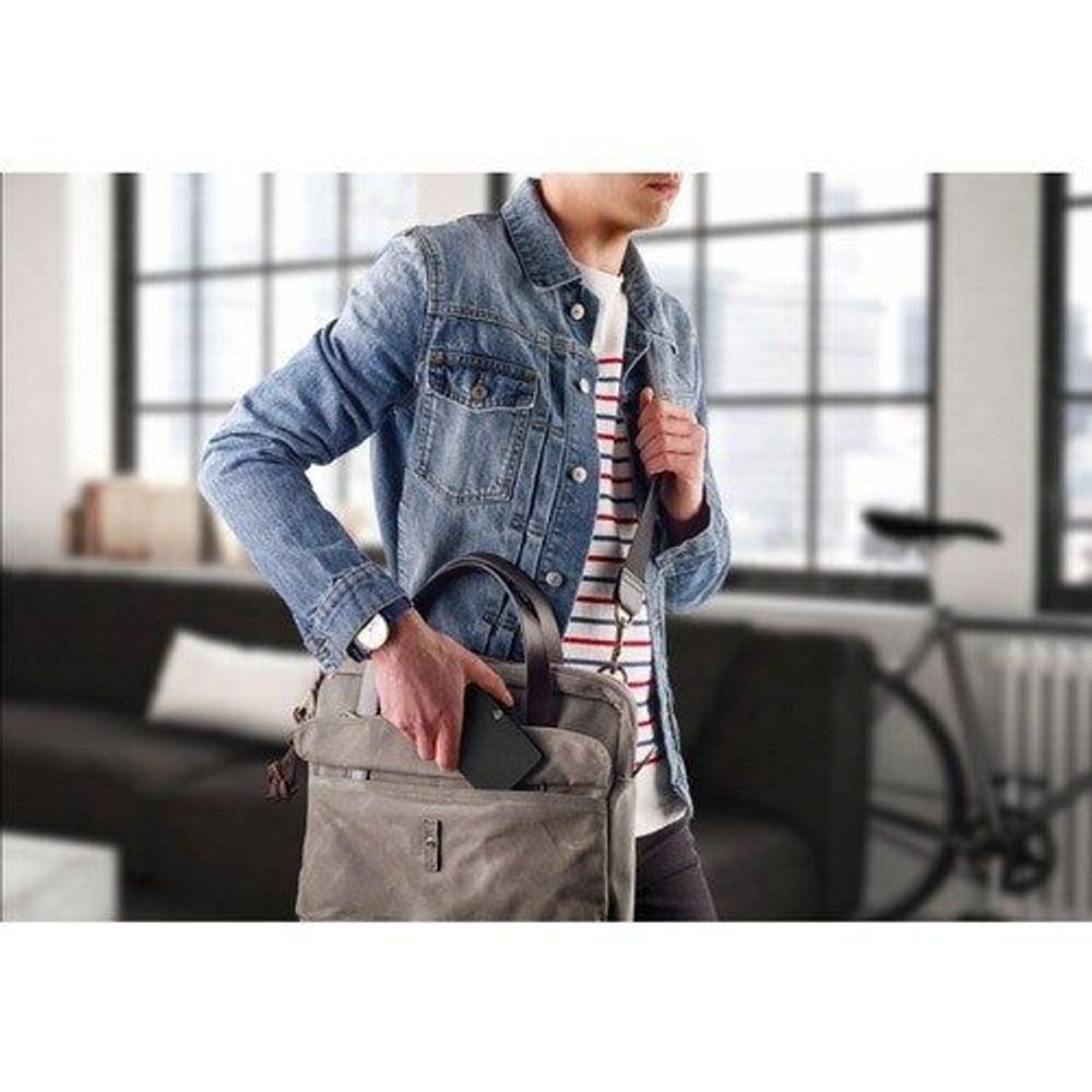 Black portable hard drive in hand as person carries a tote bag