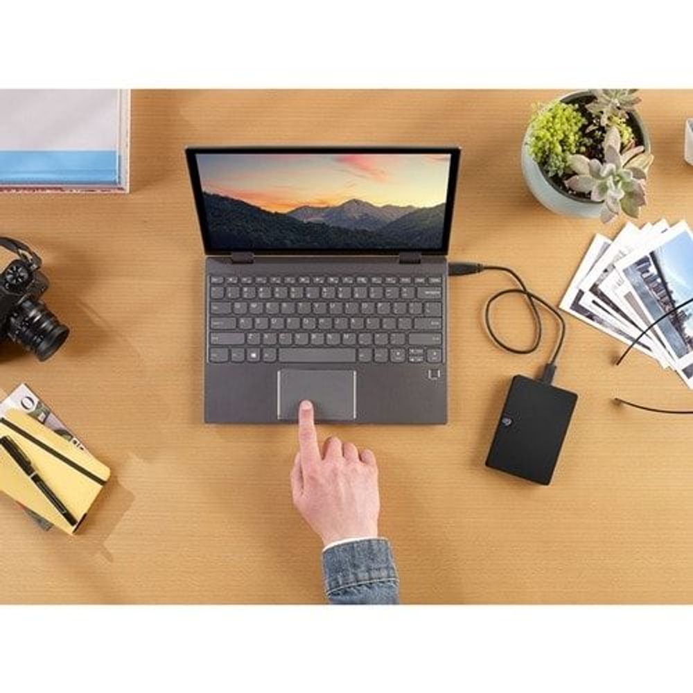Black portable hard drive connected to a laptop; hand pointing at the drive