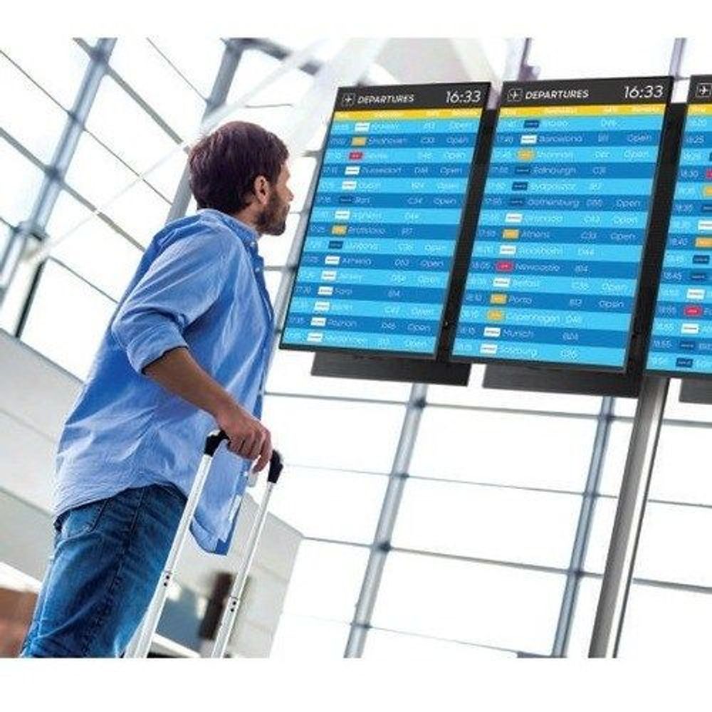 Samsung 65-inch professional LCD display showing departure timetable board
