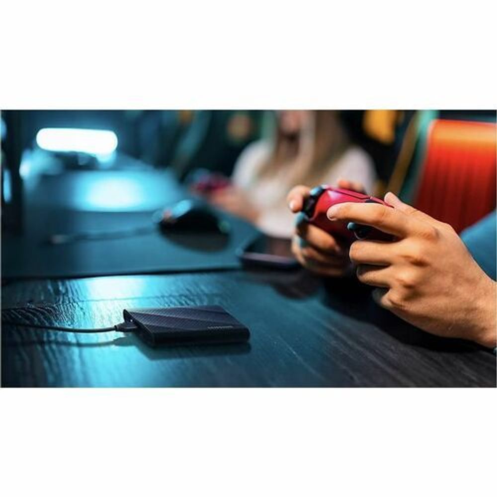 Black portable SSD with cable on tabletop near handheld device