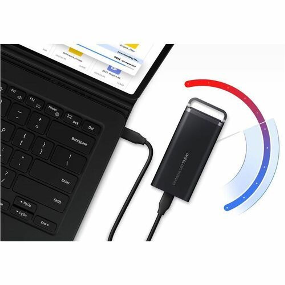 Portable SSD connected by cable to laptop keyboard, black external drive