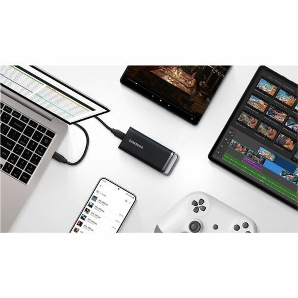 Portable SSD drive among devices on desk, black rugged design with handle