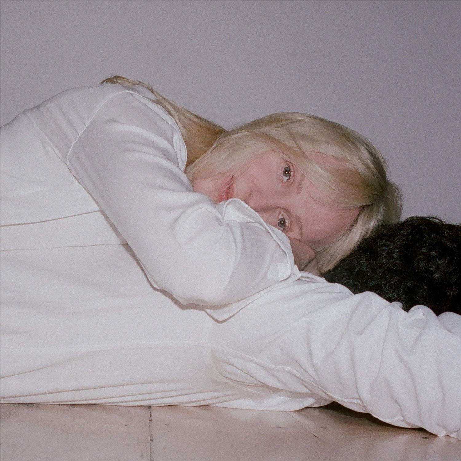 White long-sleeve shirt with soft drape, worn by a blonde person lying down