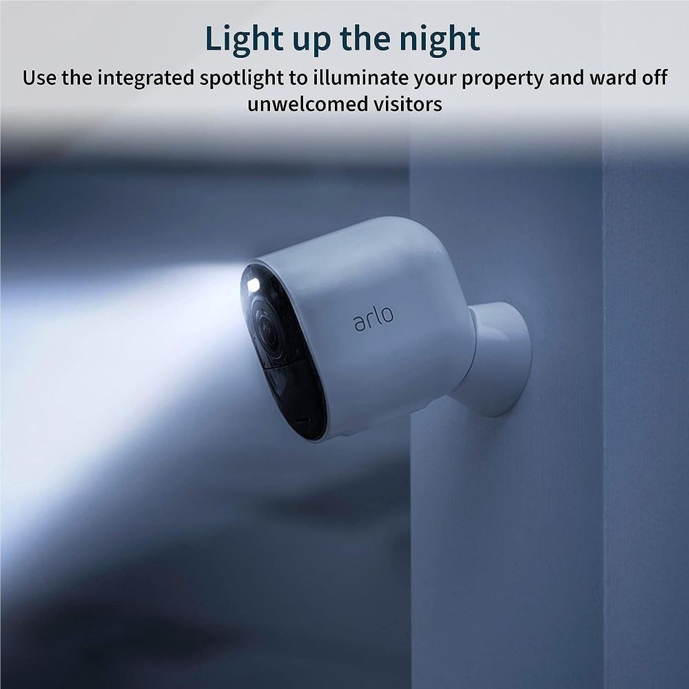 Outdoor security camera on wall with white housing and visible spotlight glow at night