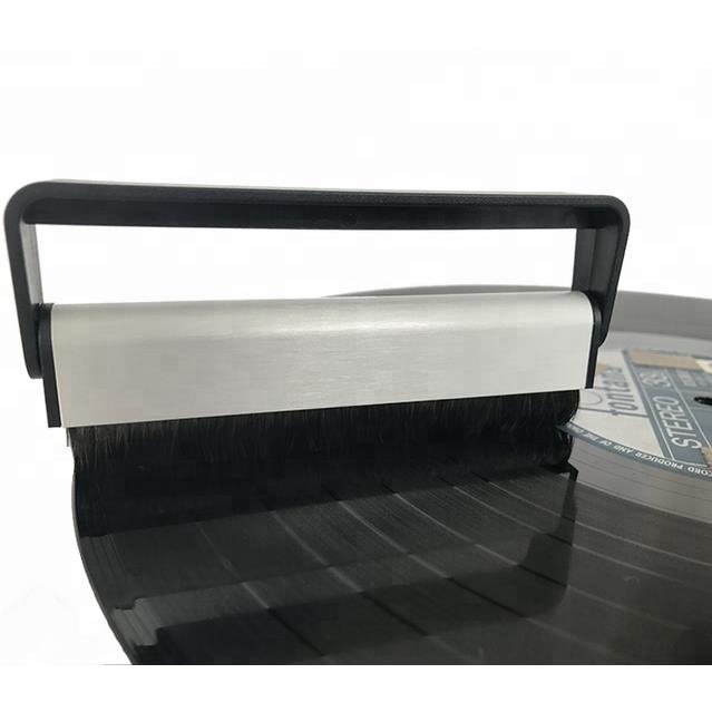 Vinyl record cleaning brush with black frame and bristle strip over a turntable record