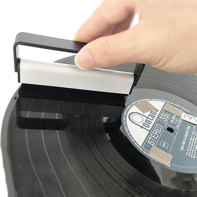 Hand holding carbon fiber cleaning brush over a vinyl record, black bristles visible