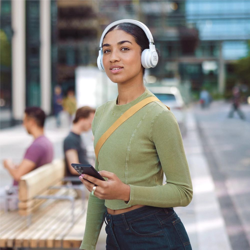 Person wearing white on-ear wireless headphones with padded headband in an outdoor street