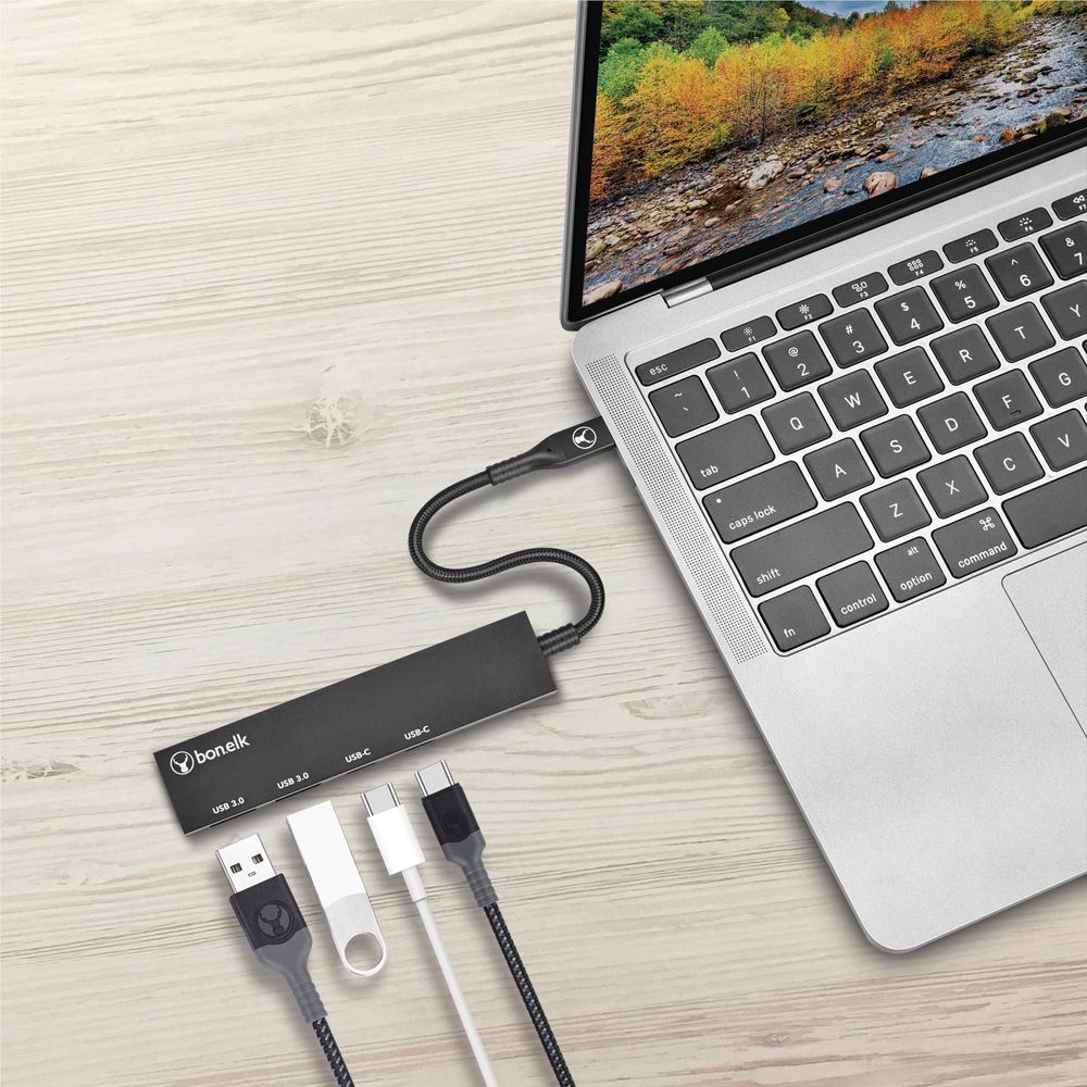 Black USB-C hub connected to a laptop on a desk with included adapters