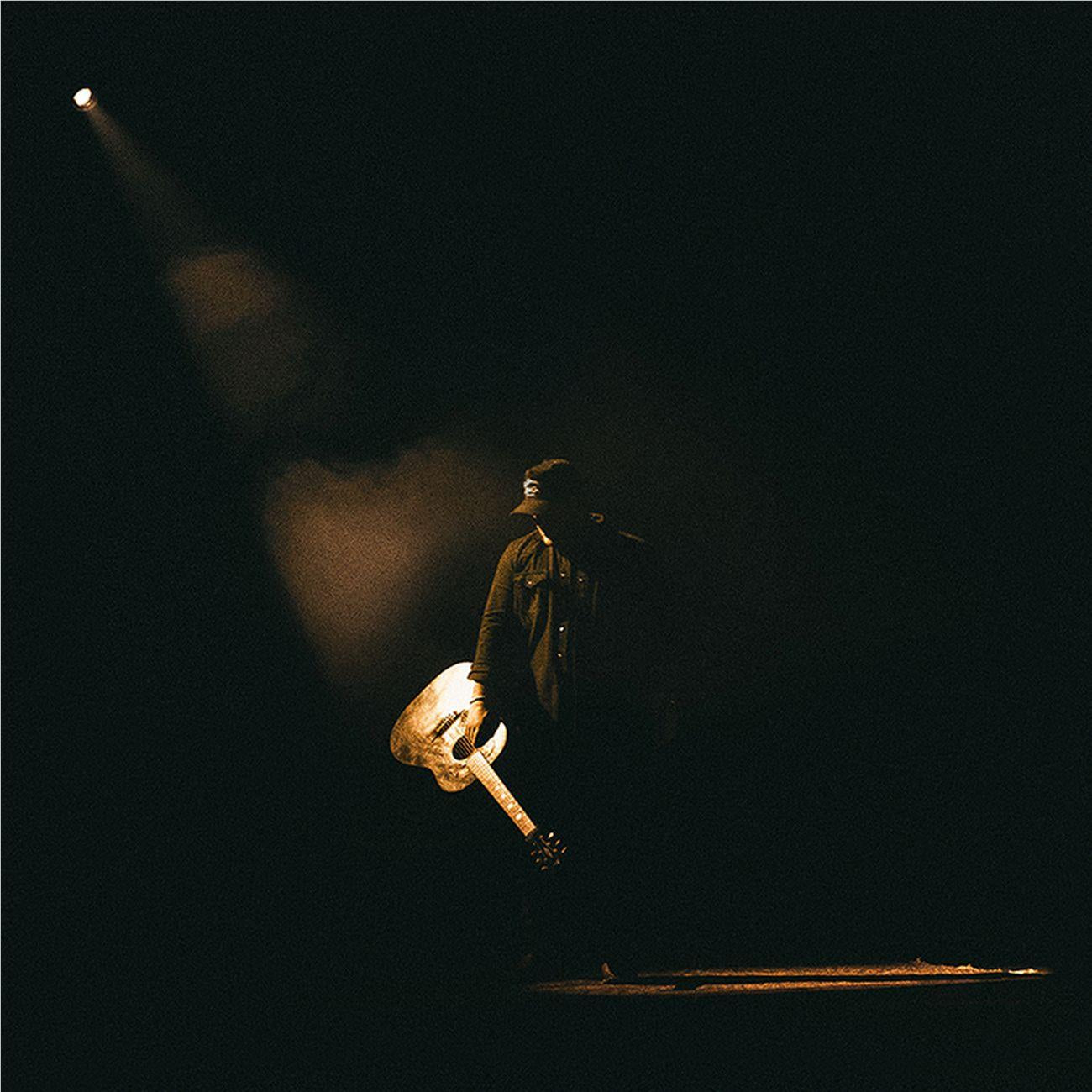 Male singer holding a guitar, standing on stage