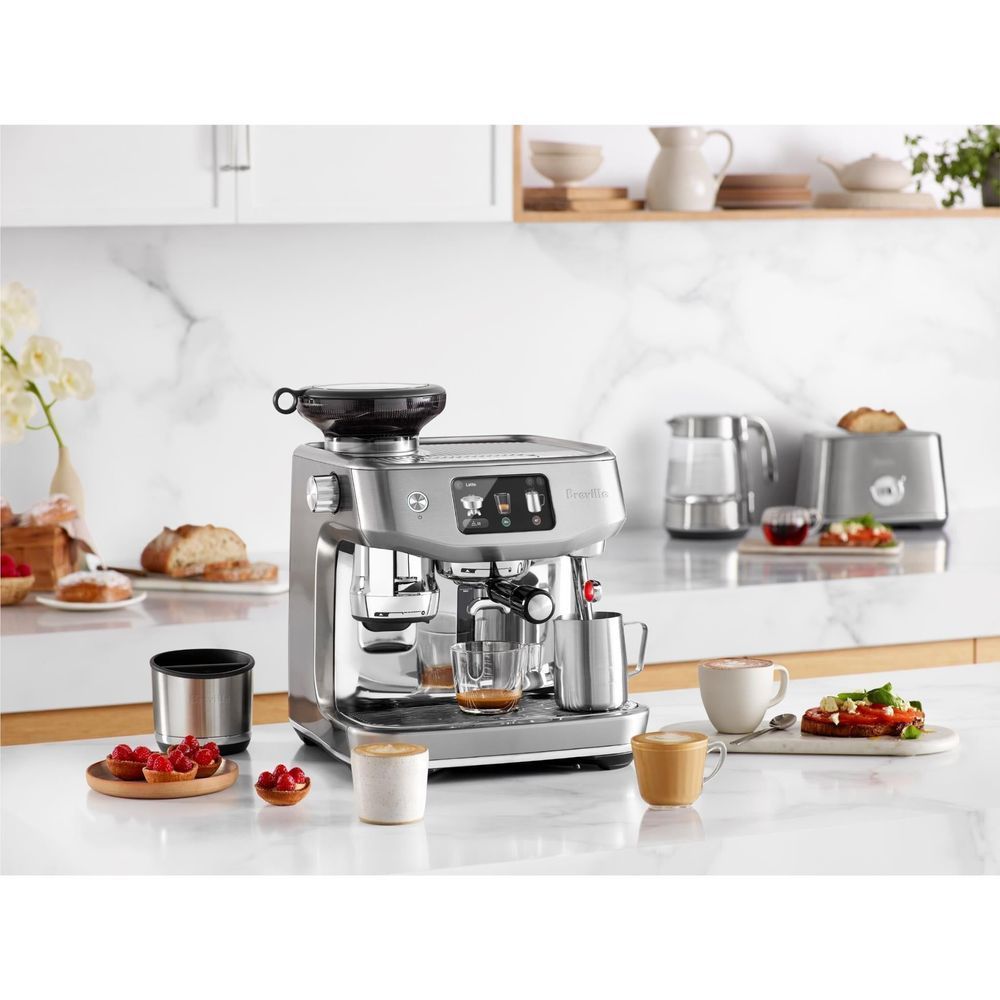 Stainless steel espresso machine on countertop with milk pitcher and coffee cups