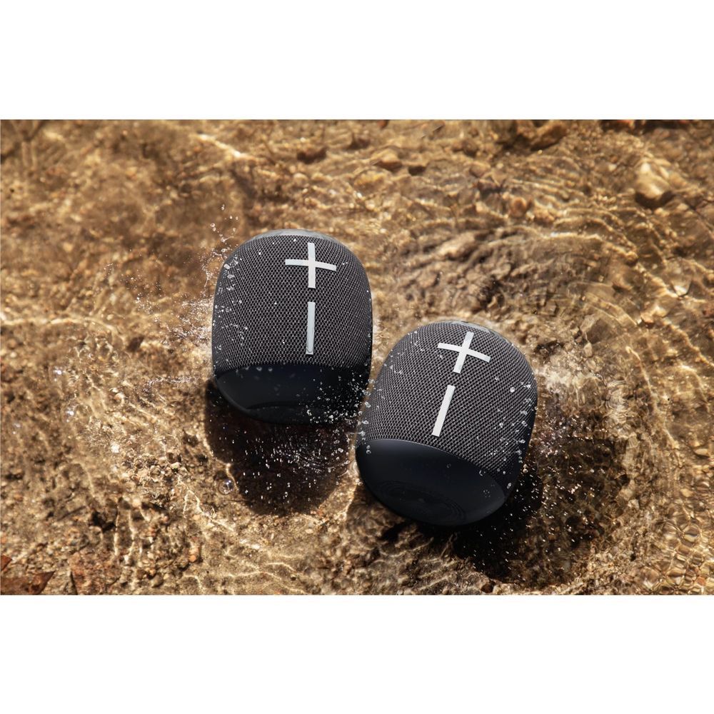 Pair of black portable Bluetooth speakers with plus icons on wet rocks