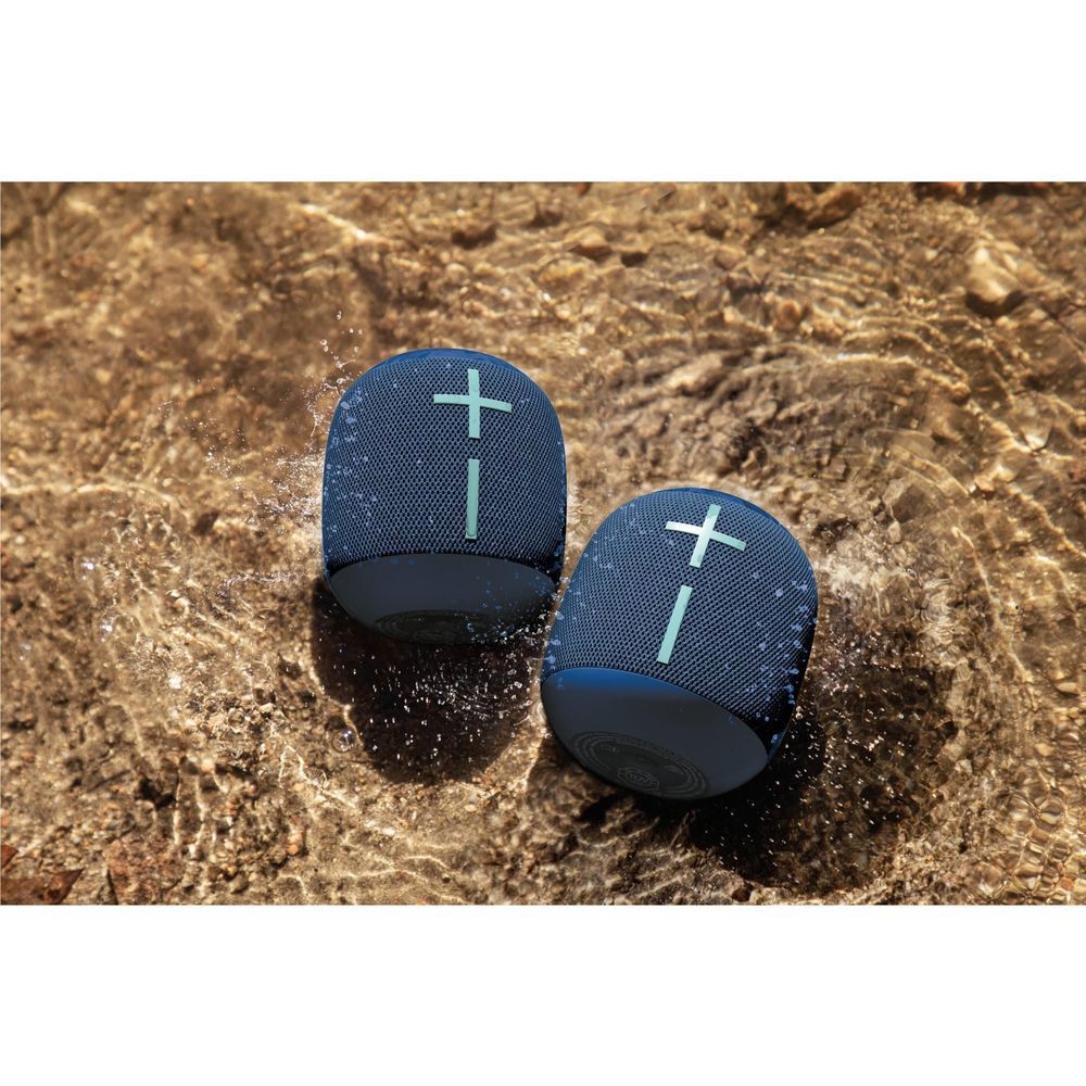 Pair of cobalt blue portable Bluetooth speakers with fabric mesh, in splashing water
