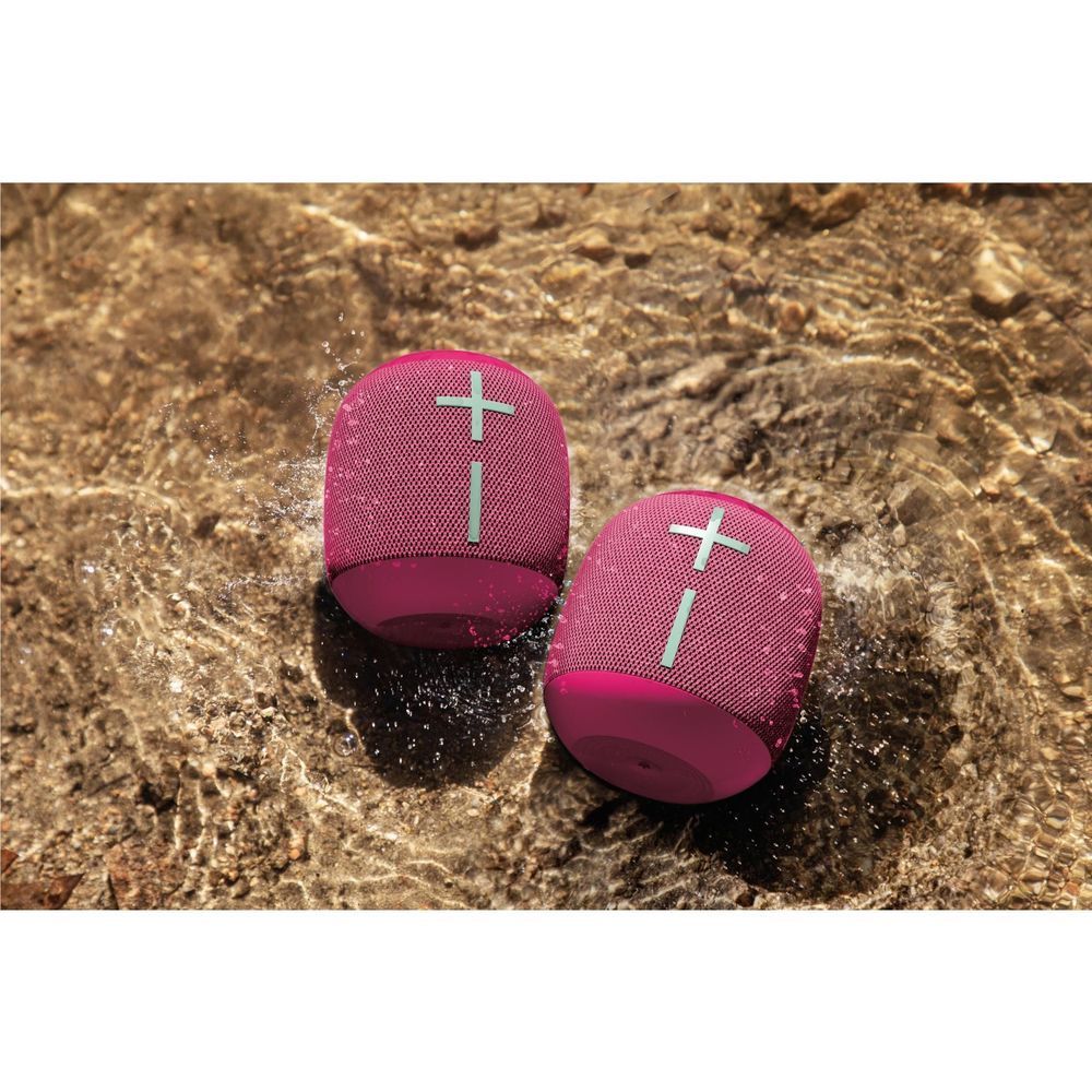 Two Hyper Pink portable Bluetooth speakers on wet surface, mesh plus tops