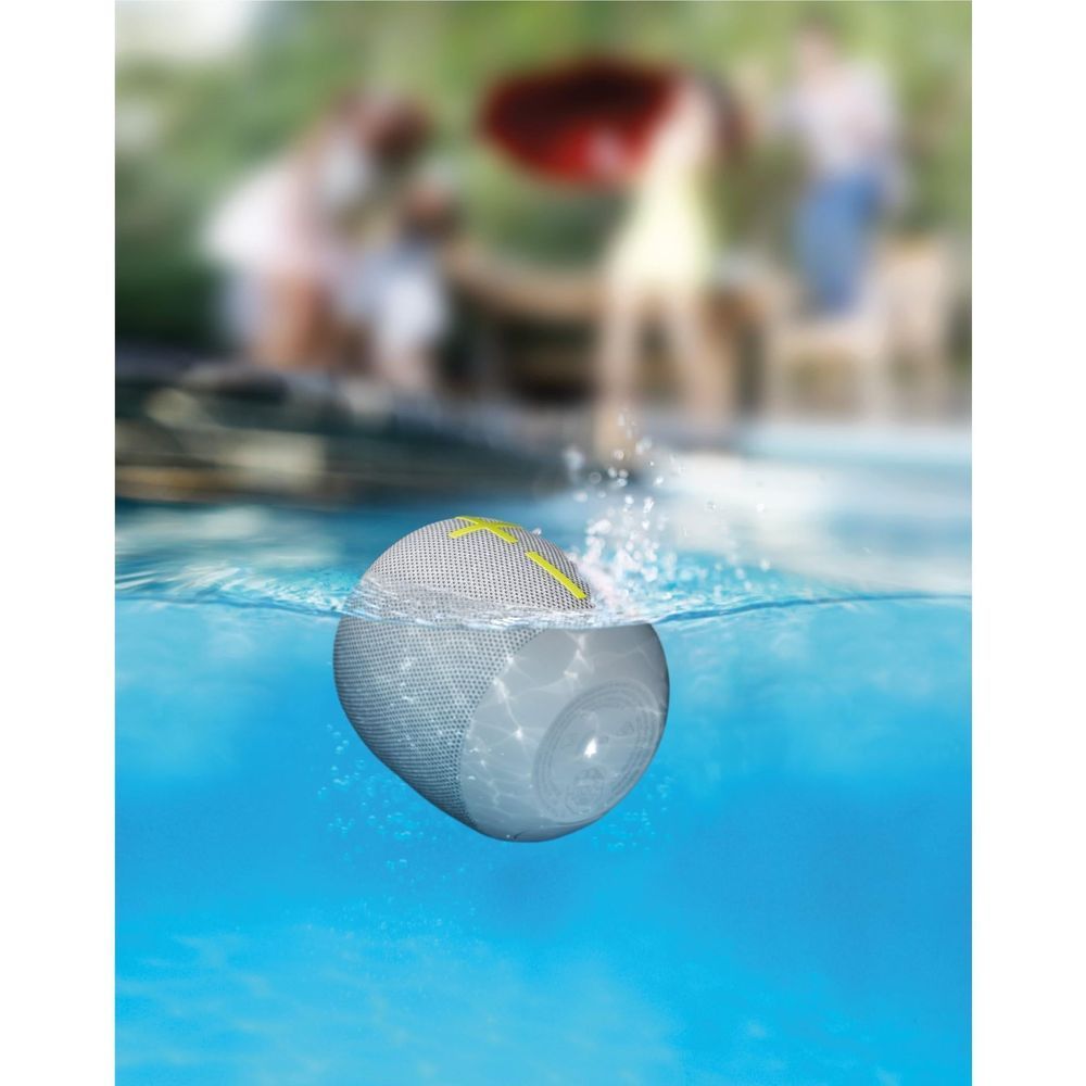 Gray portable Bluetooth speaker with lime handle in water, yellow plus marking visible