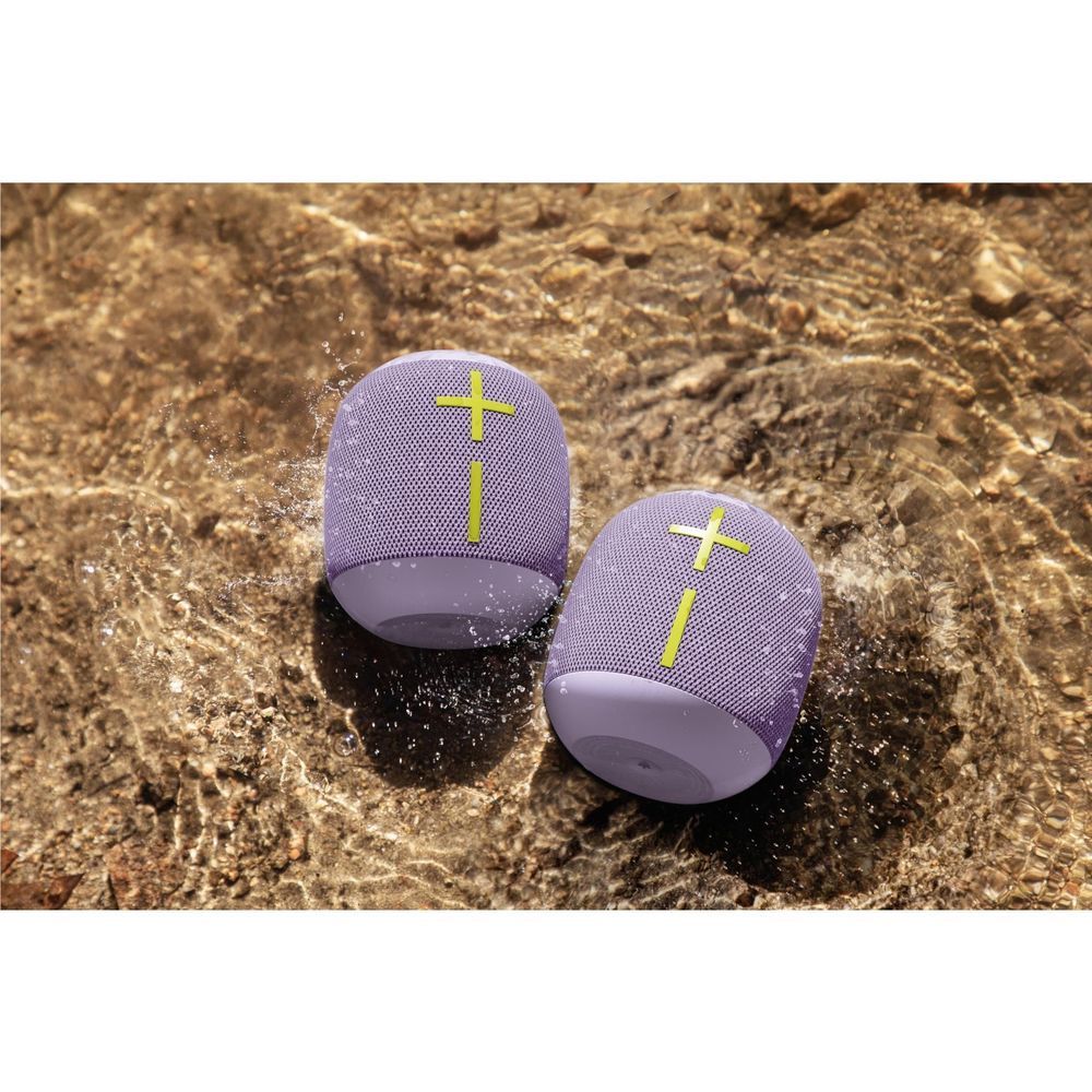 Two lilac portable Bluetooth speakers with lime straps, shown with water splashes on rock