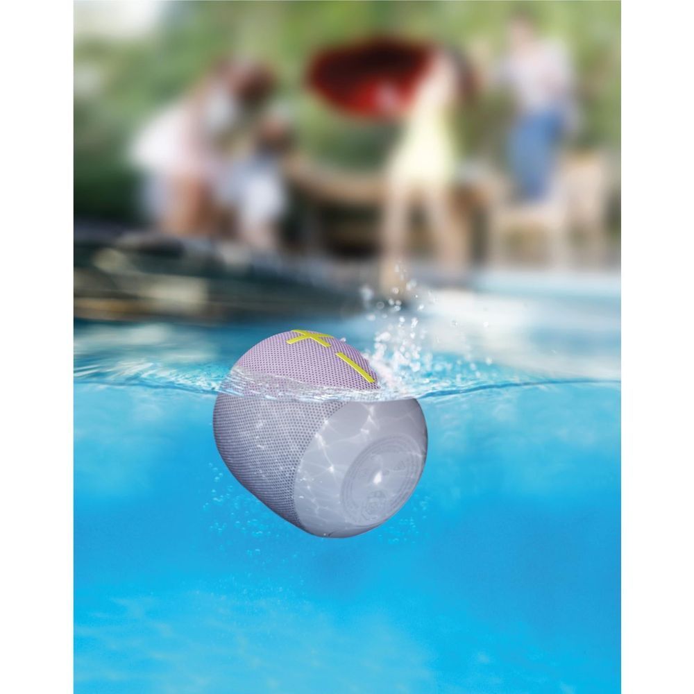 Lilac portable Bluetooth speaker with lime strap floating in water, splash side view