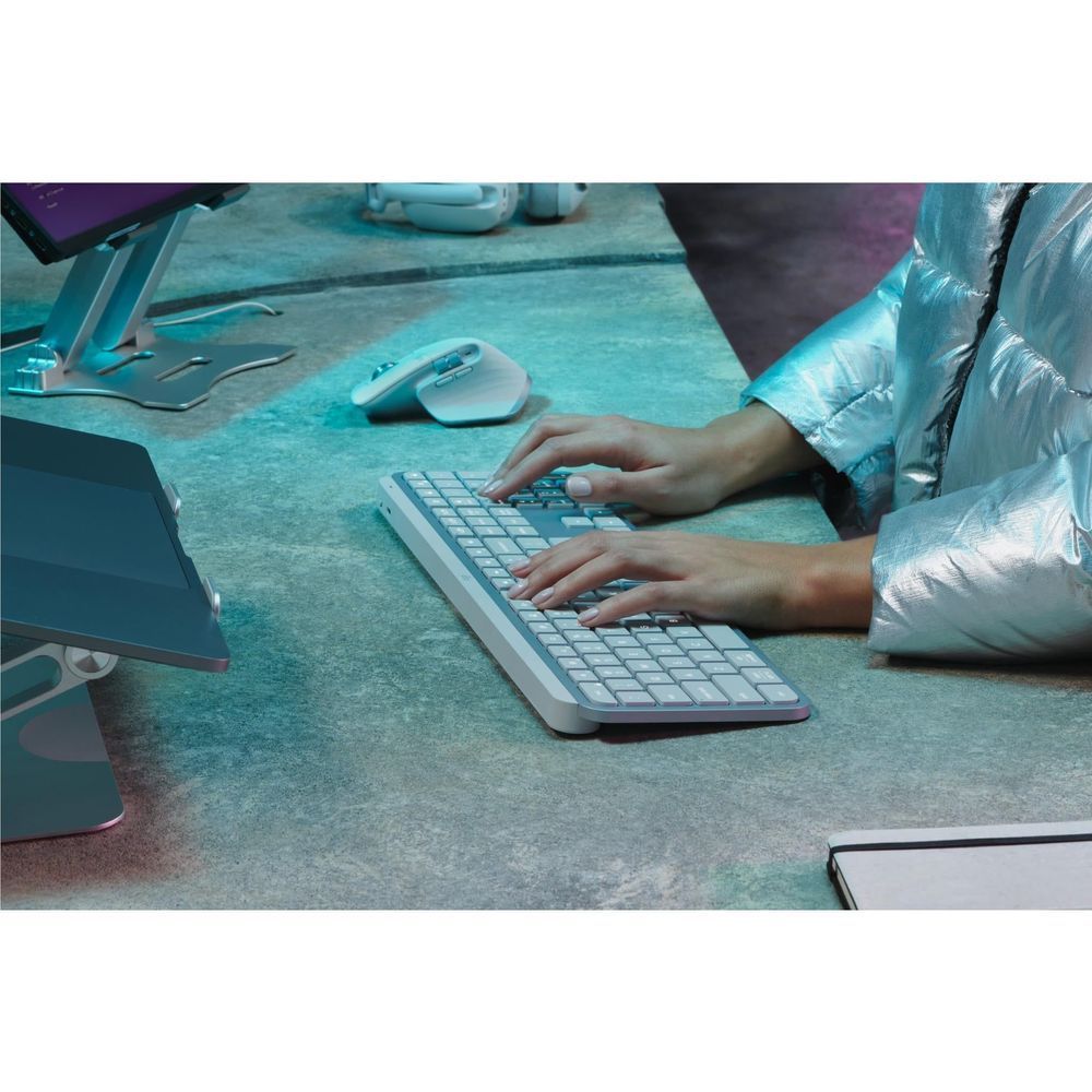Pale grey wireless illuminated keyboard, hands typing on the illuminated keys