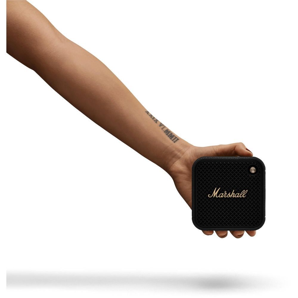 Black portable Bluetooth speaker in hand, showing front grille and gold “Marshall” logo