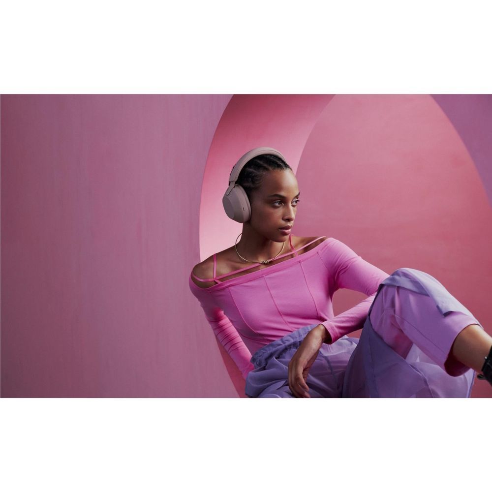 Smokey pink over-ear wireless headphones worn by a person in a pink long-sleeve top