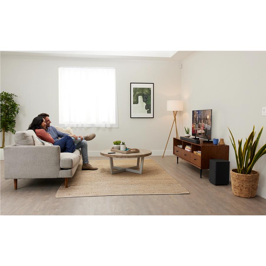 Living room scene with black soundbar and wireless subwoofer on the floor.