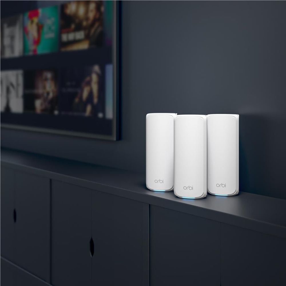 Three white Orbi mesh WiFi router pods standing on a shelf