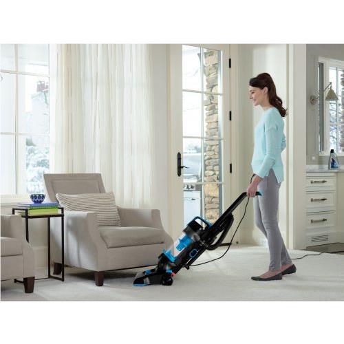 Bagless upright vacuum cleaner with brush head and hose, pushed across carpet