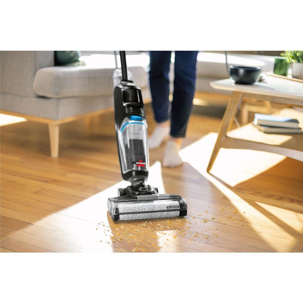 Upright wet and vacuum hard floor cleaner scrubbing wood floors, black with blue tank.
