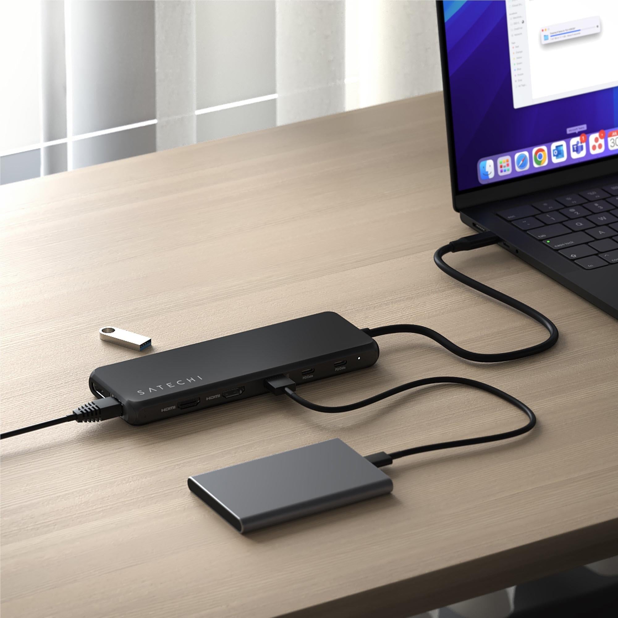 Black USB-C multiport hub with ports connected on wooden desk, cables visible