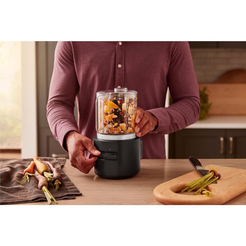 KitchenAid food chopper on counter with hands using the clear-lidded bowl