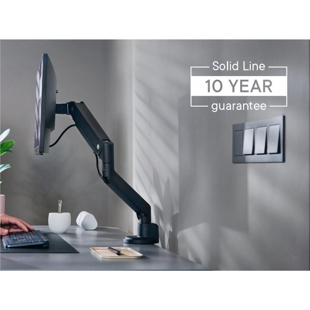 Black single monitor arm installed on desk, holding monitor above workspace