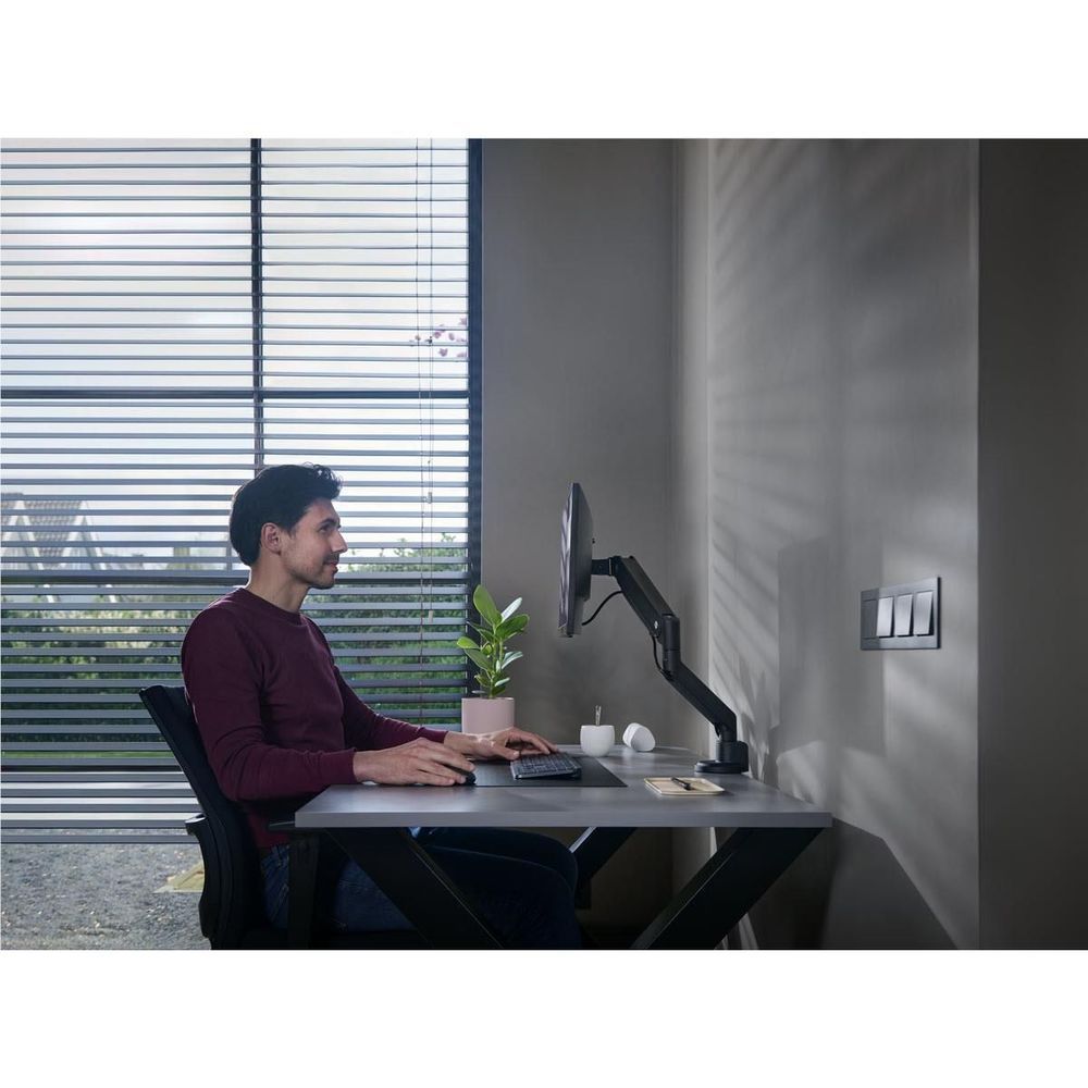 Black single monitor arm with wall mount, holding a monitor over desk area