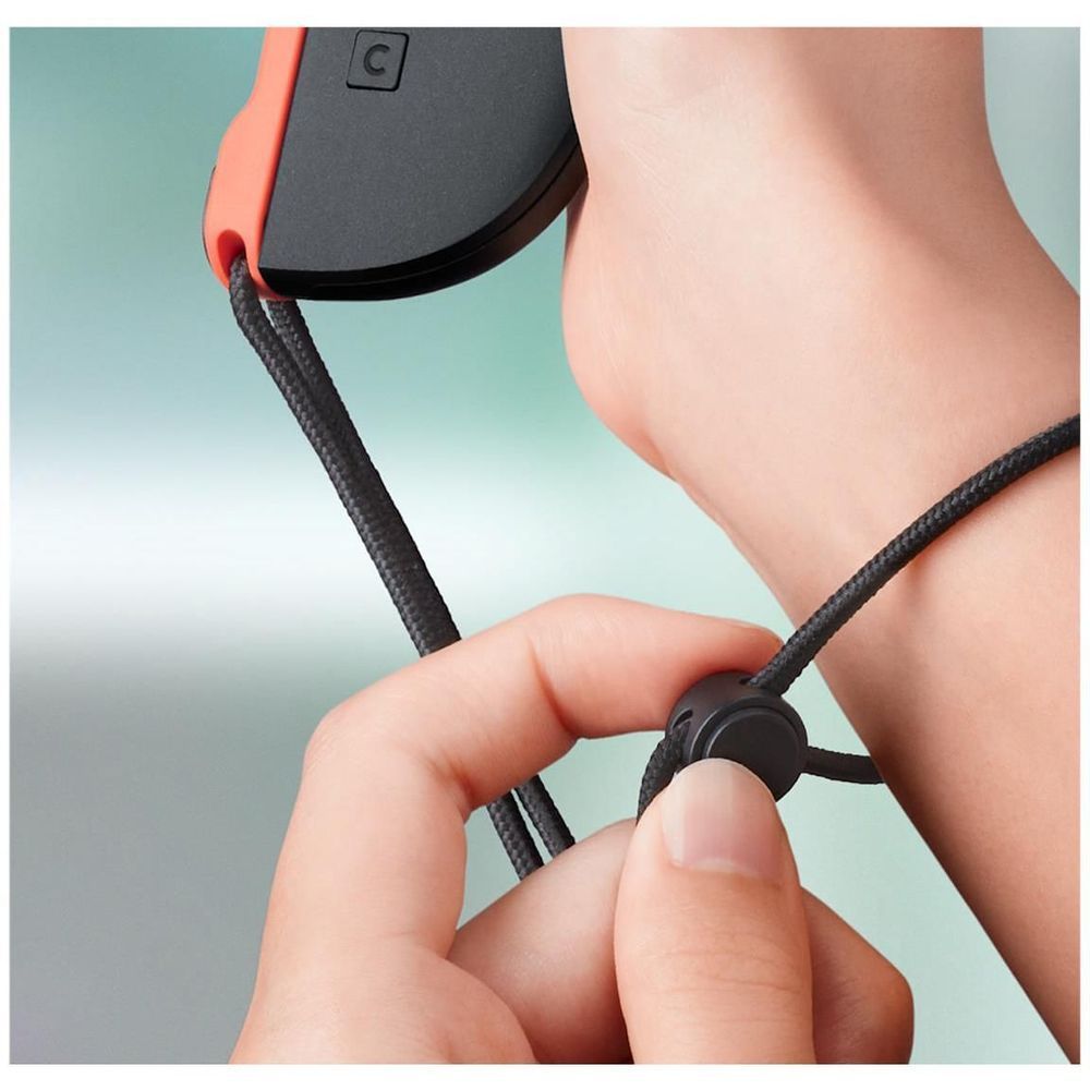 Hand fastening a black connector on a light red Joy-Con wrist strap with braided cord