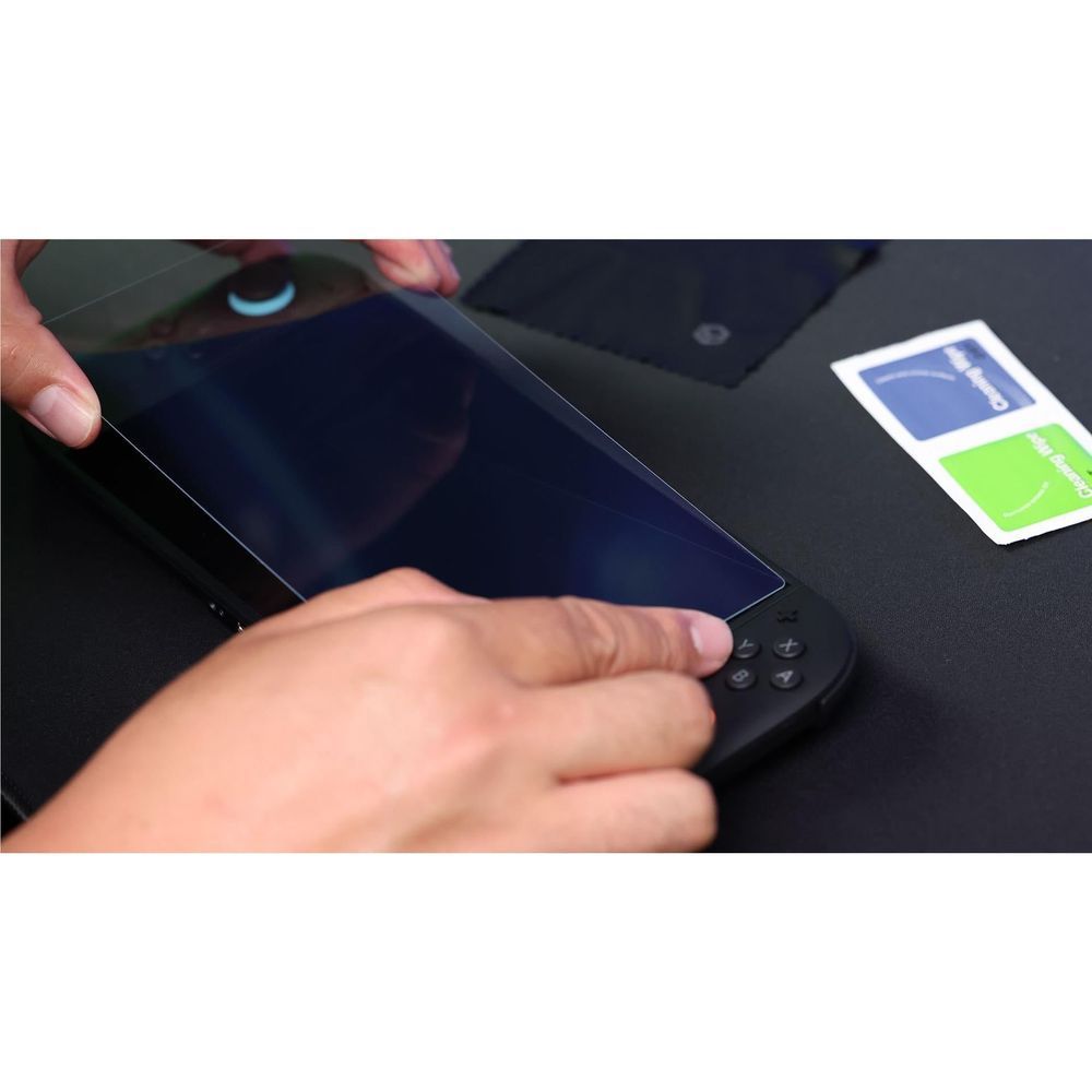 Hands pressing tempered glass screen protector onto handheld console screen
