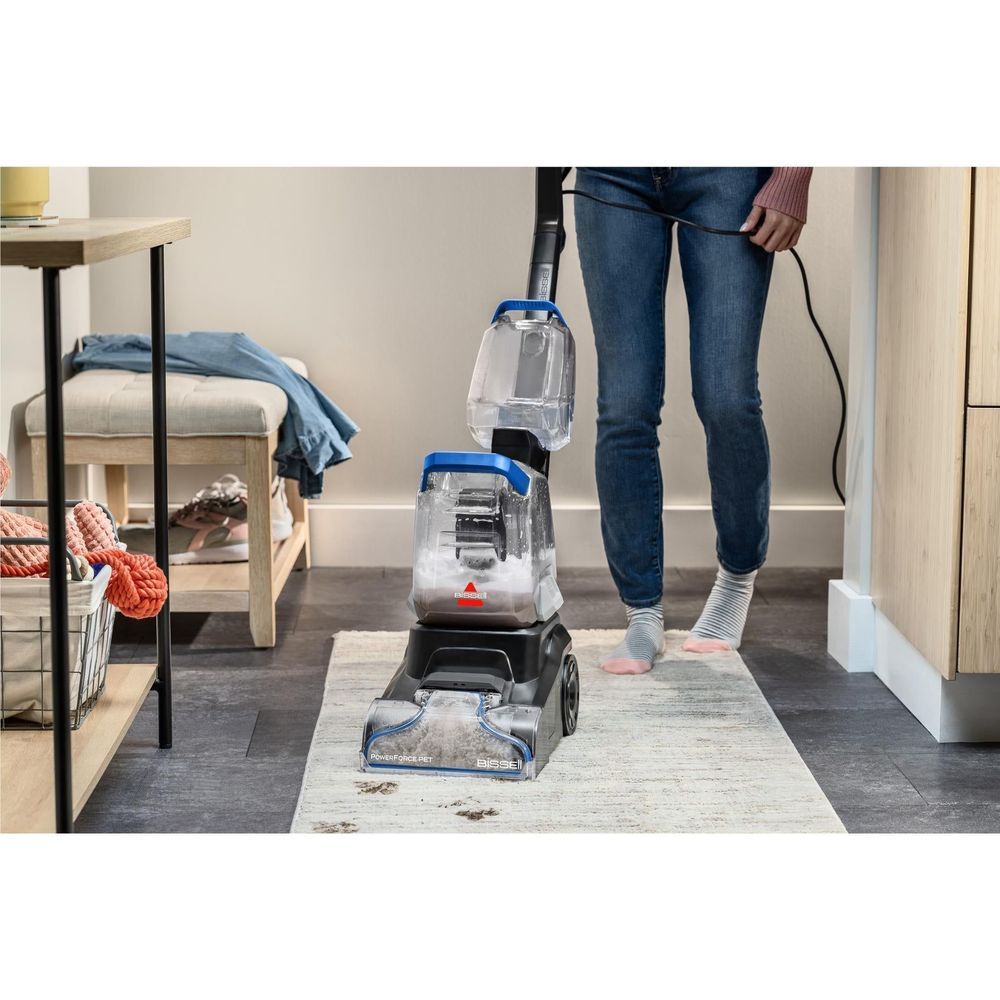 Upright carpet cleaner in use on an area rug; blue-tipped cleaning head dispensing