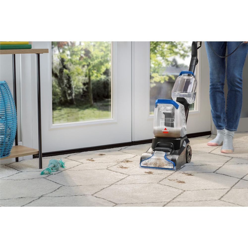 Upright cleaner with wide head treating stains on a light rug near a door