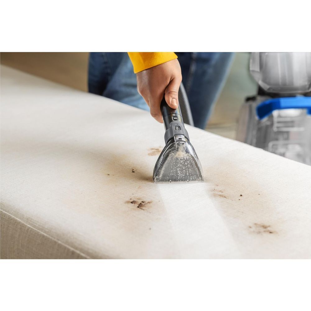 Compact nozzle tool cleaning a light couch cushion with visible dirt extraction