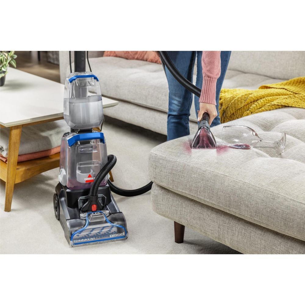 Upright carpet cleaner with hose using an upholstery nozzle on a light fabric sofa