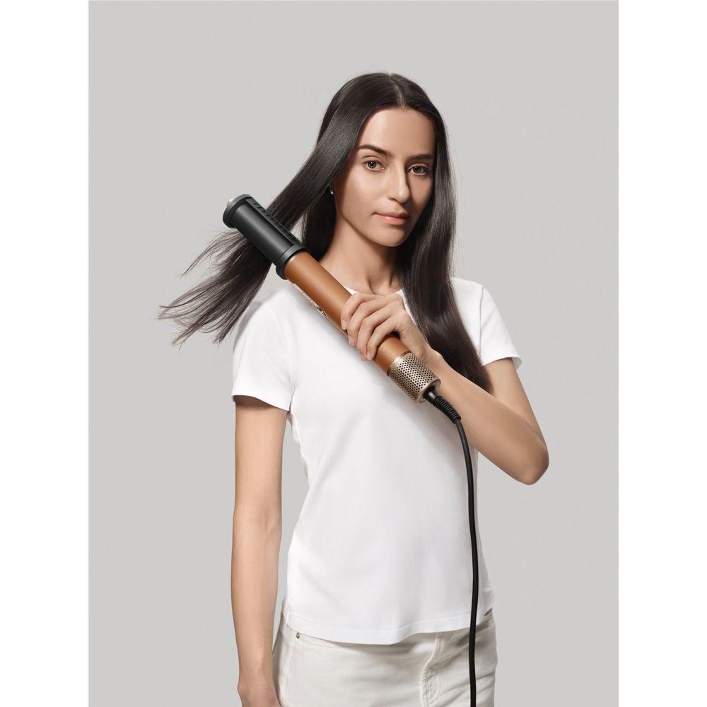 Bronze hair dryer styling tool held near hair, with black attachment