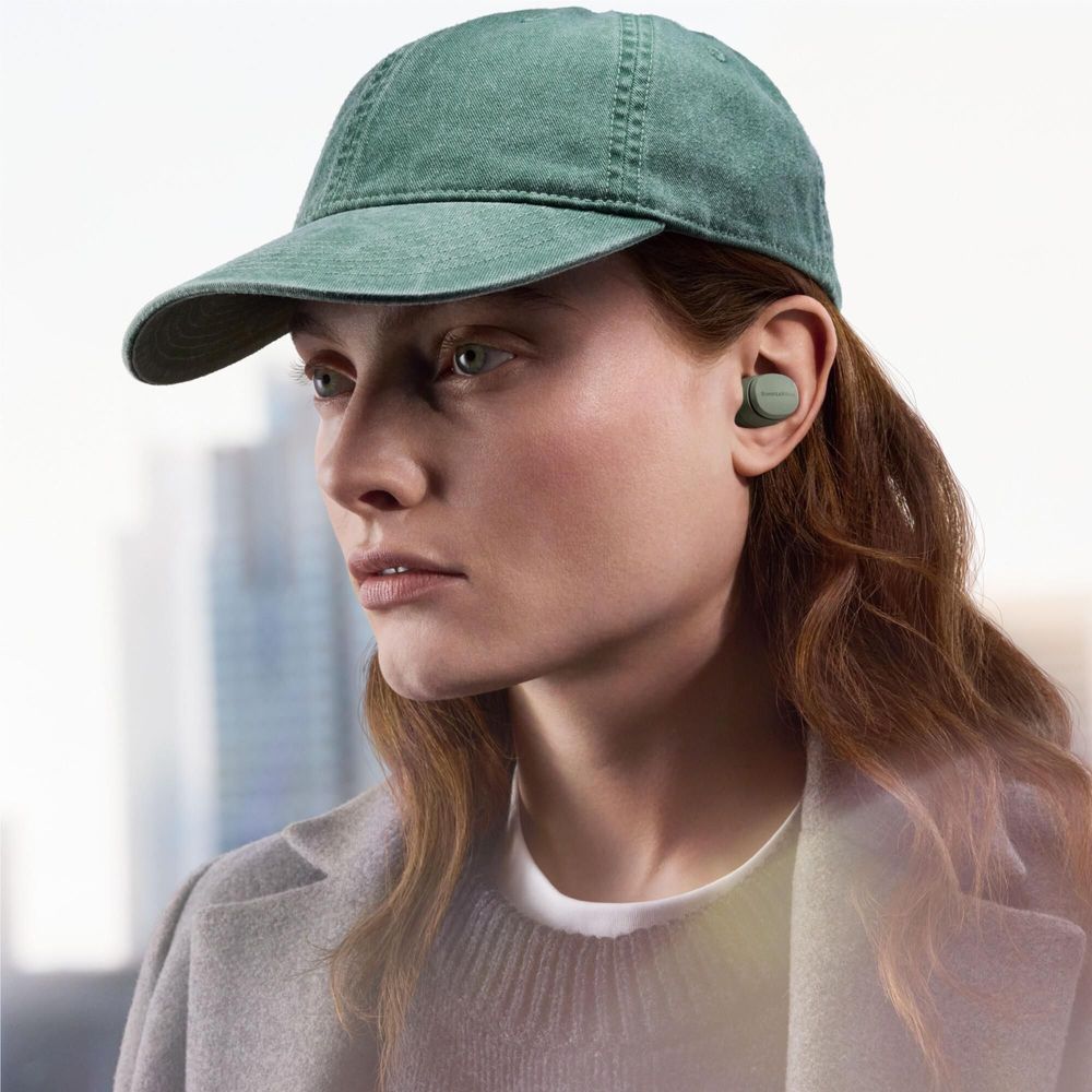Forest green in-ear earbuds on ear with green cap and sweater
