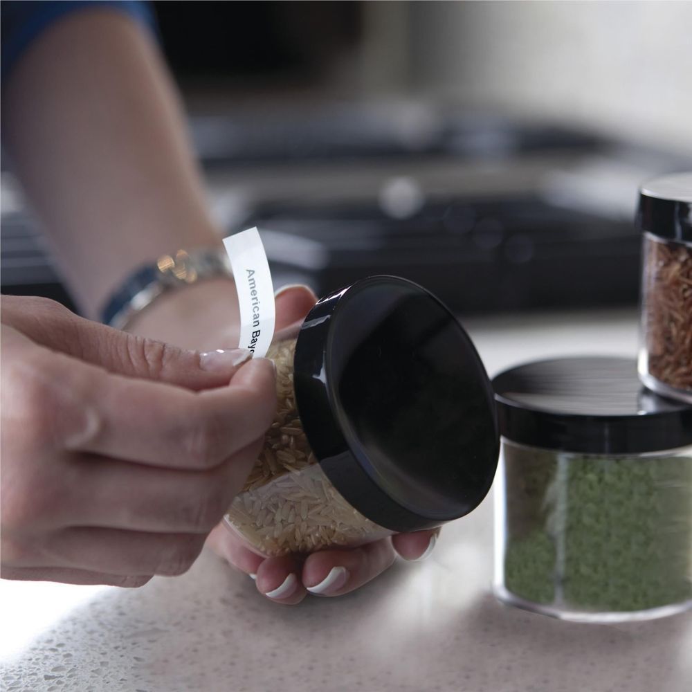 Hand applying a white label tape strip to a container using a label maker