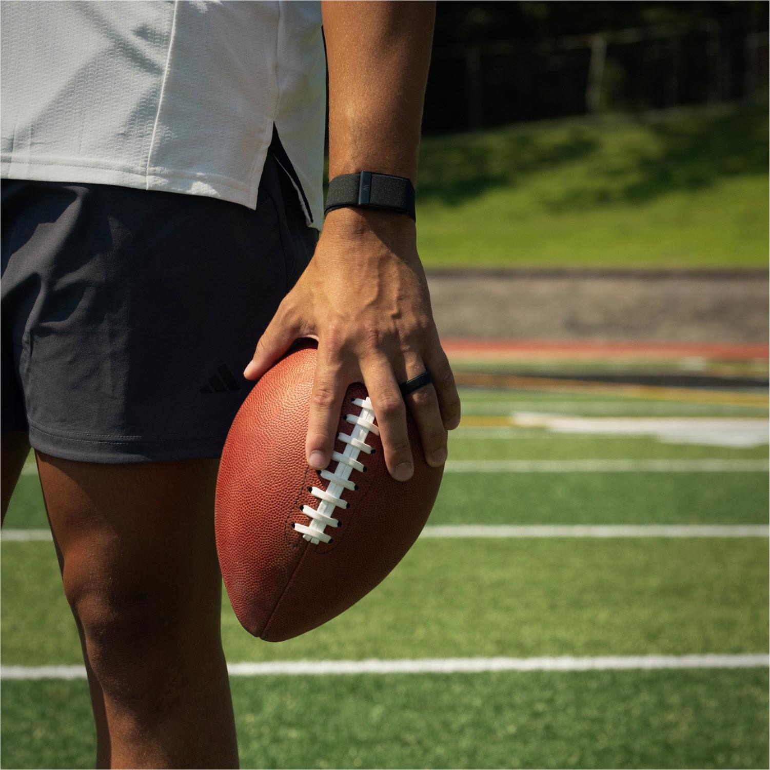 Man wearing a black health tracker band on wrist while holding a football