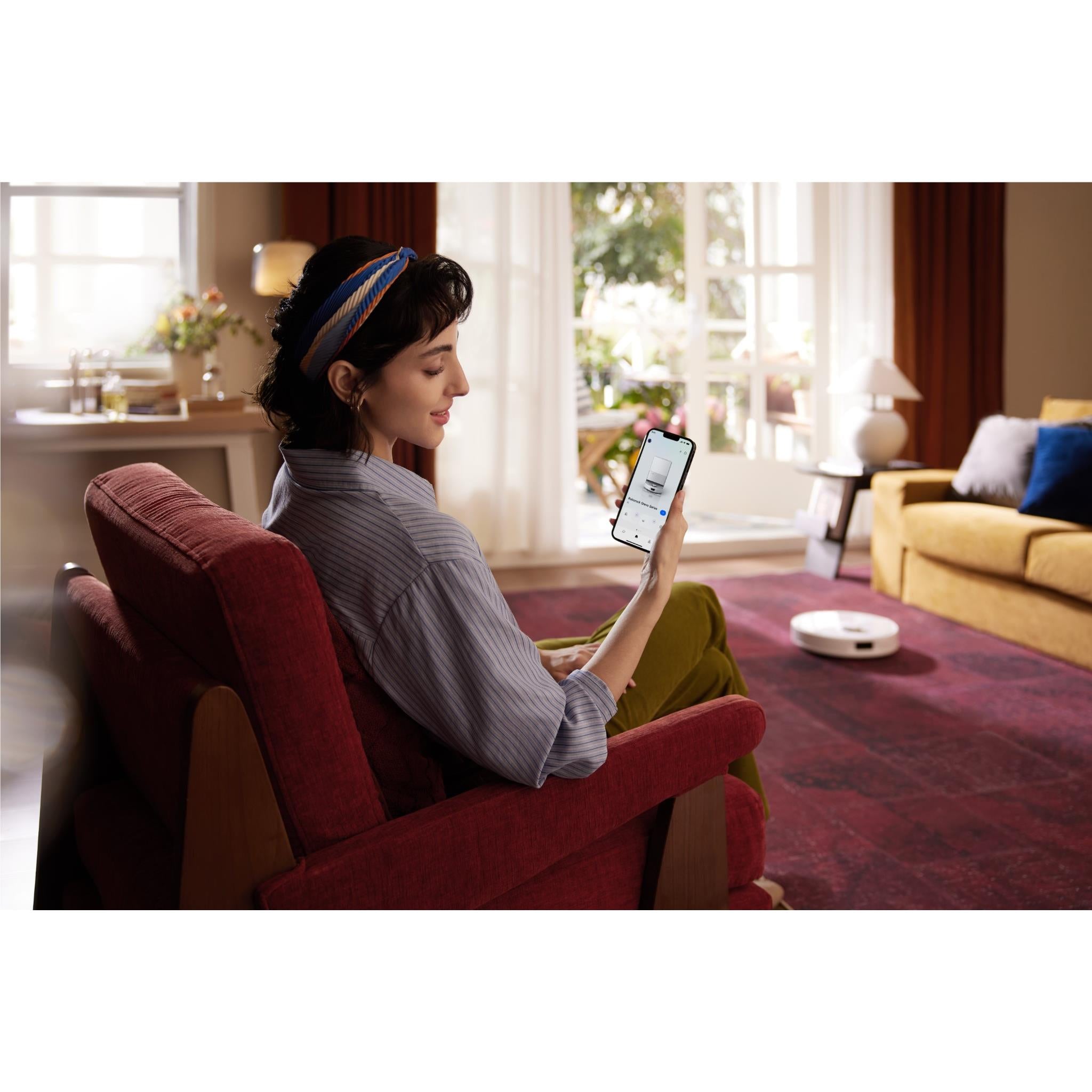 White robot vacuum and mop controlled on a smartphone app in a living room.