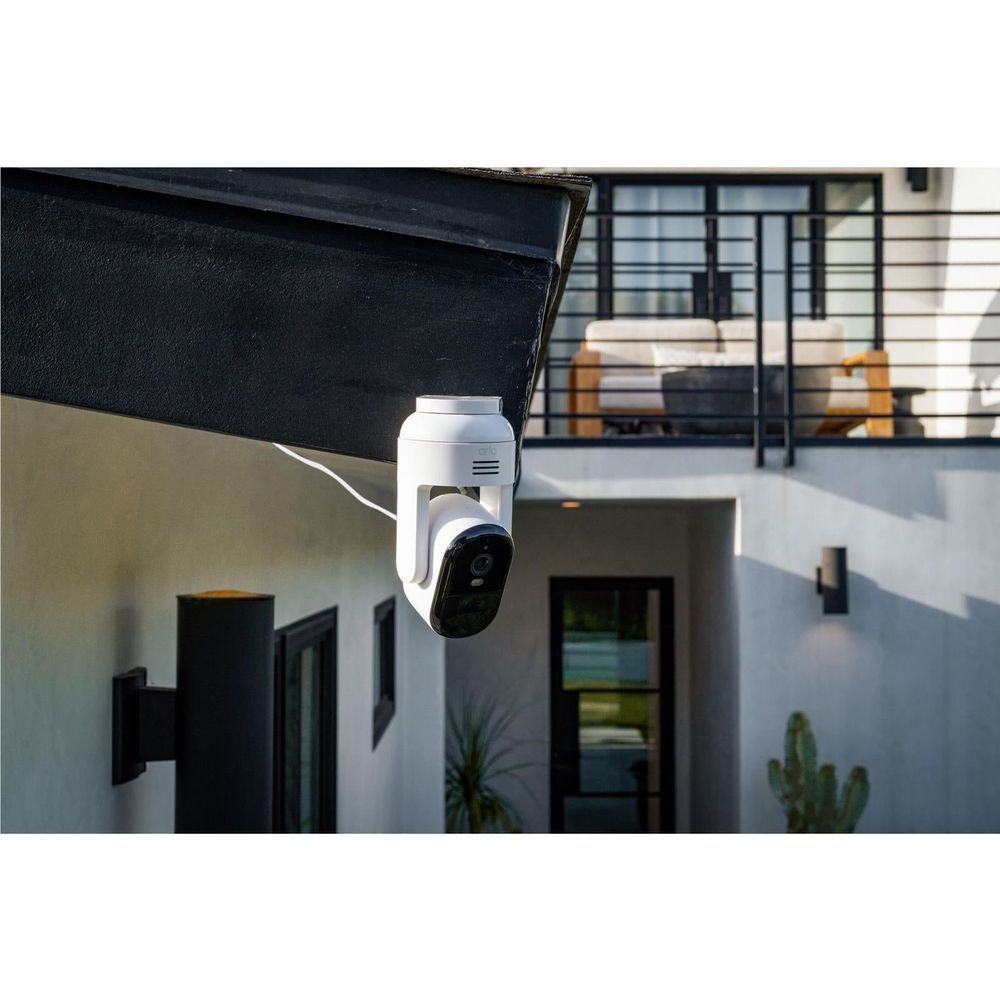 White outdoor pan-tilt security camera mounted under a roof eave